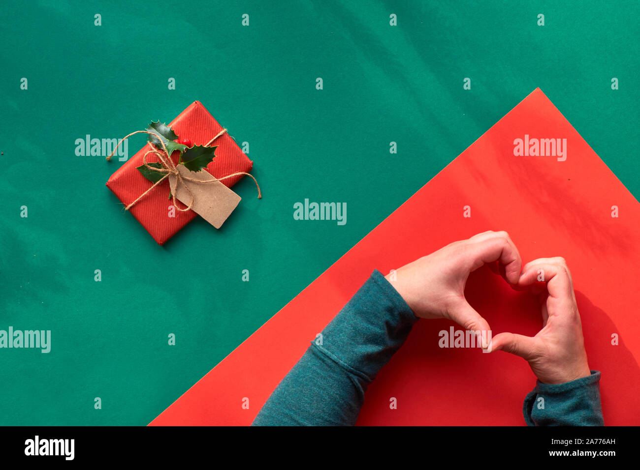 Kreative diagonal Geometrische flach an der grünen und roten Papier mit langen floralen Schatten. Verpackt Geschenkkarton dekoriert mit Holly. Hände mit Herz anmelden Stockfoto