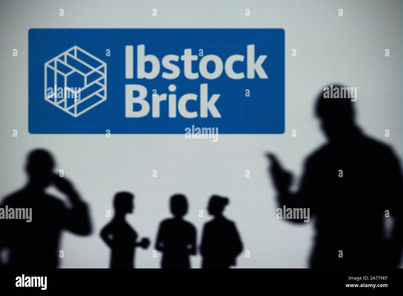 Die ibstock Brick Logo ist auf einen LED-Bildschirm im Hintergrund, während eine Silhouette Person ein Smartphone verwendet (nur redaktionelle Nutzung) Stockfoto