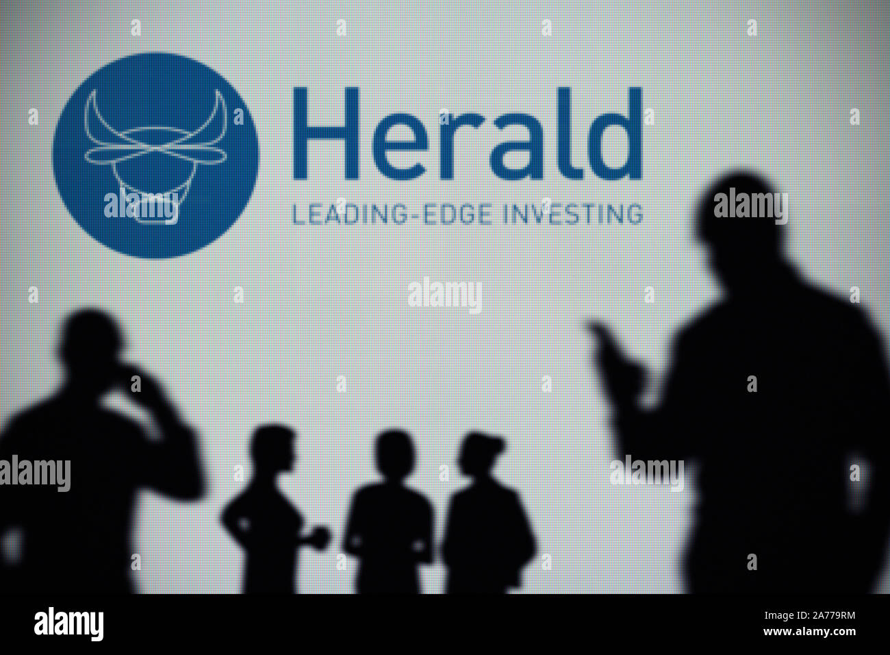 Der Herald Investment Trust Logo ist auf einen LED-Bildschirm im Hintergrund, während eine Silhouette Person ein Smartphone verwendet (nur redaktionelle Nutzung) Stockfoto