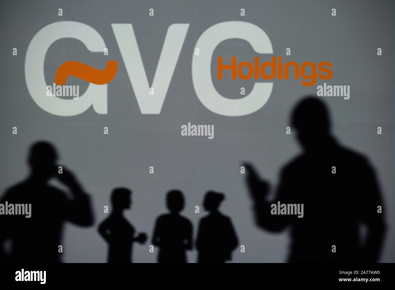 Die GVC Betrieben Logo ist auf einen LED-Bildschirm im Hintergrund, während eine Silhouette Person ein Smartphone verwendet (nur redaktionelle Nutzung) Stockfoto