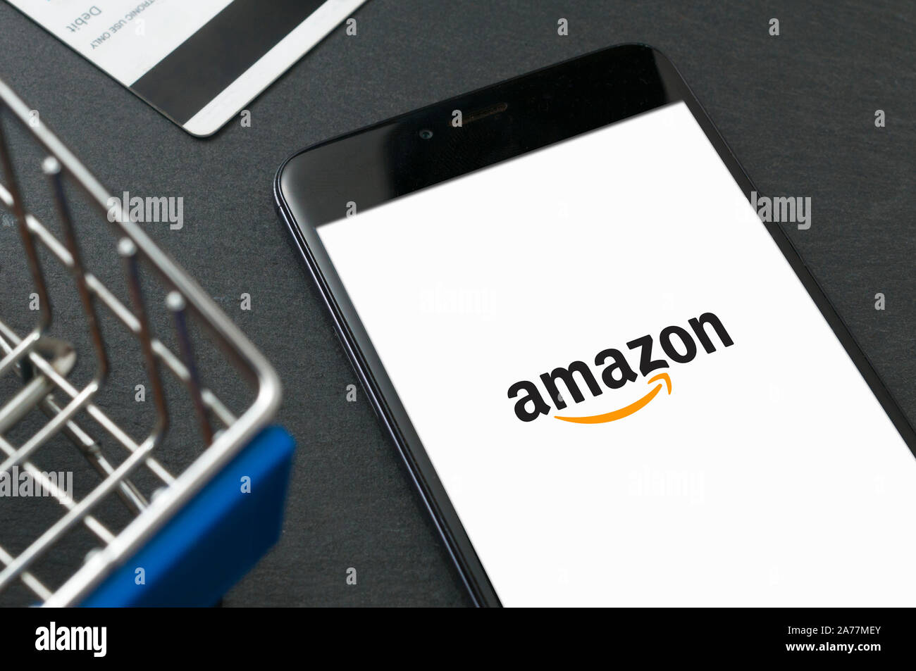 Carrara, Italien - 31. Oktober 2019 - Smartphone mit Amazon Logo auf dem Bildschirm auf einen Tisch in der Nähe auf ein Spielzeug Warenkorb und eine EC-Karte. Amazon ist die w Stockfoto