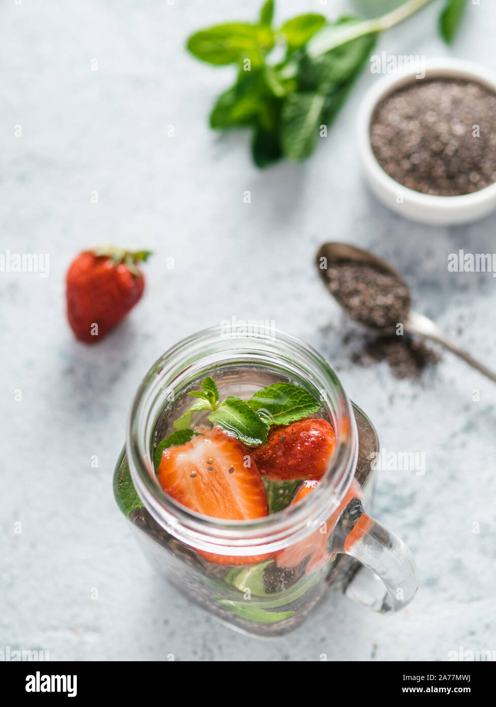 Ansicht von oben Chia Wasser im Marmeladenglas mit Erdbeere und Minze auf grauzement Hintergrund. Chia infundiert detox Wasser mit Beeren. Gesunde Ernährung, Getränke, Ernährung, Entgiftung Konzept. Vertikale Stockfoto