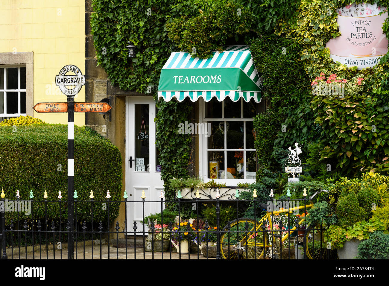 Die Außenseite des malerisch einladenden sonnigen Efeu bewachsenen Dalesman Café Teestube & Süße Emporium (weiß Eingang Tür) - Gargrave, North Yorkshire, England, Großbritannien Stockfoto