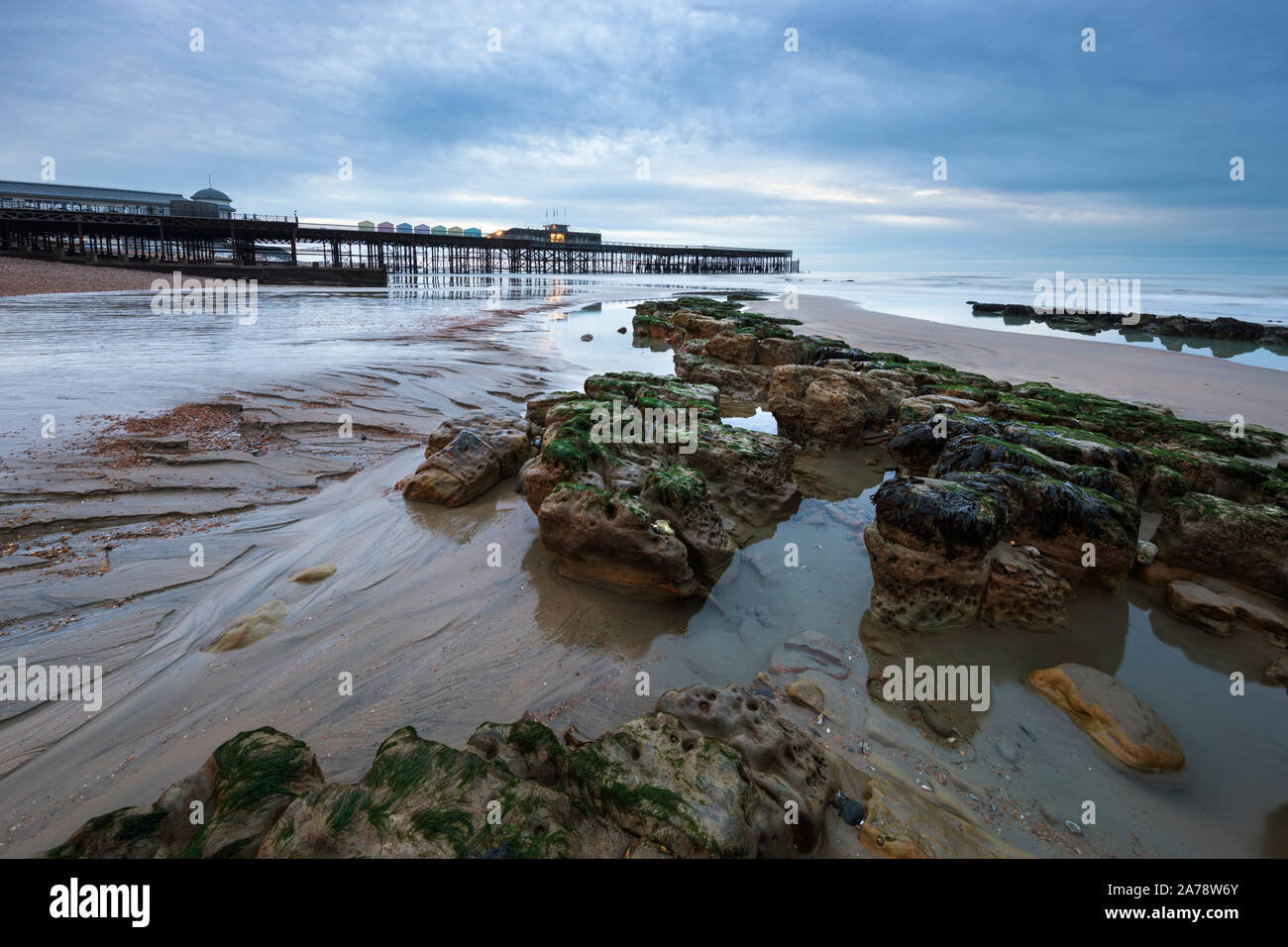 Hastings Pier mit Felsen am Strand bei Ebbe in der Morgendämmerung, Hastings, East Sussex, England, Vereinigtes Königreich, Europa Stockfoto