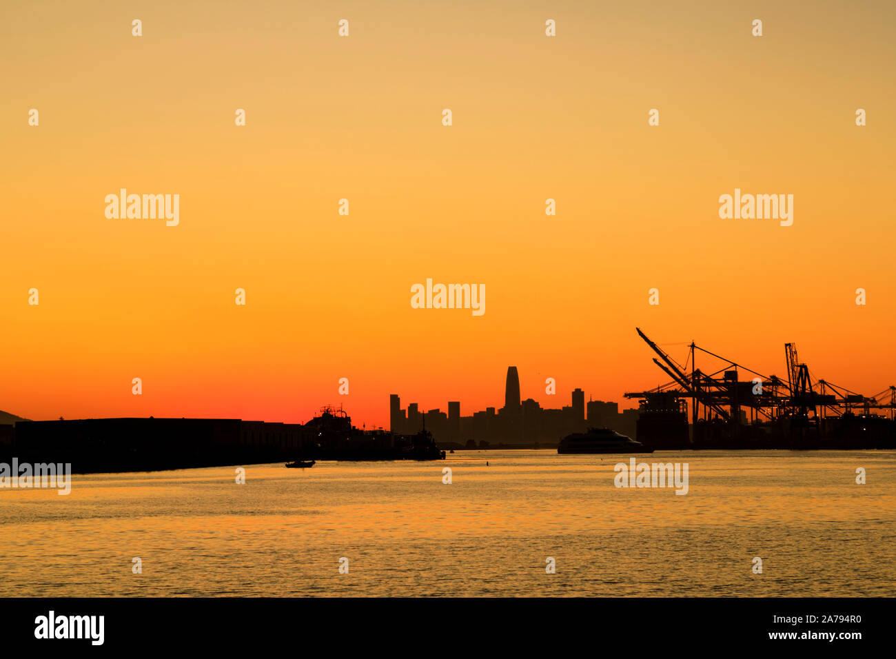 Sonnenuntergang über der Skyline von San Francisco und den schweren Liftkranen von Oakland Port, Oakland, Kalifornien Stockfoto