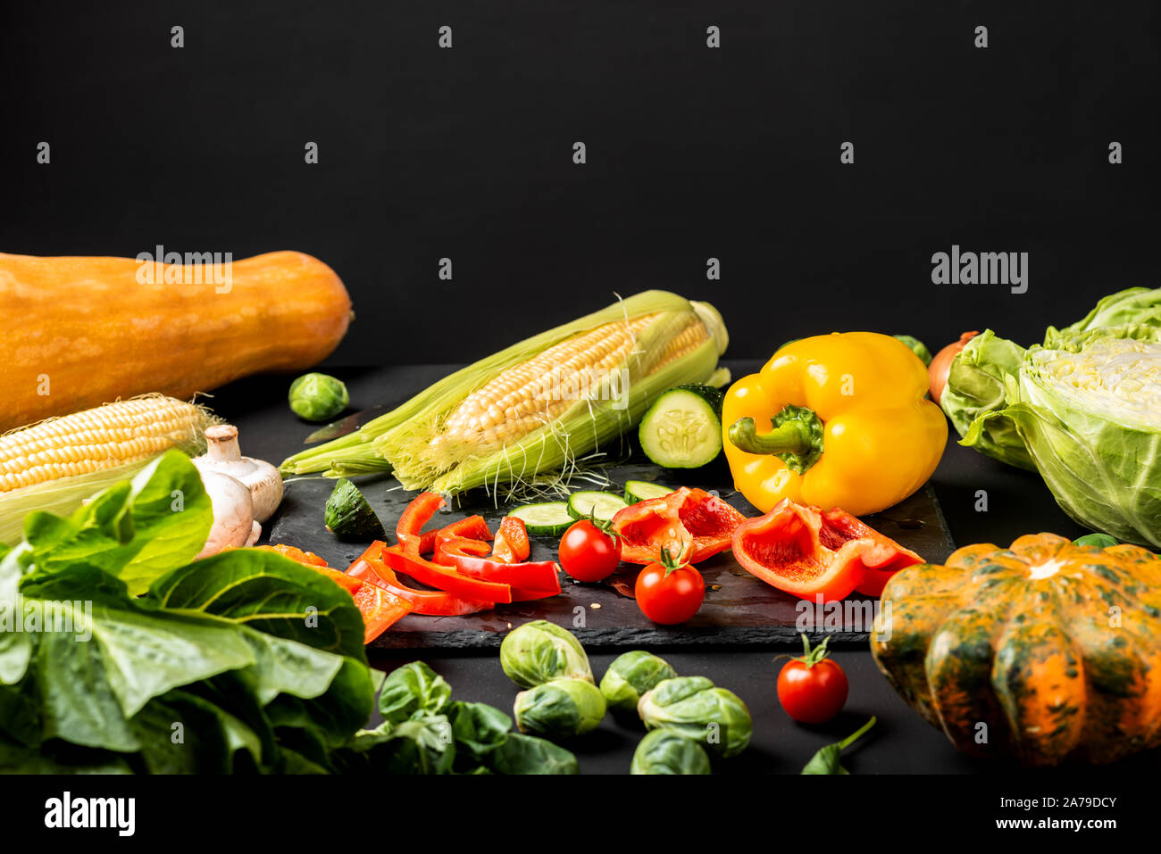 Gehacktes Gemüse auf einem schwarzen Brett und anderes frisches Gemüse auf einem Schwarzen Tisch. Stockfoto