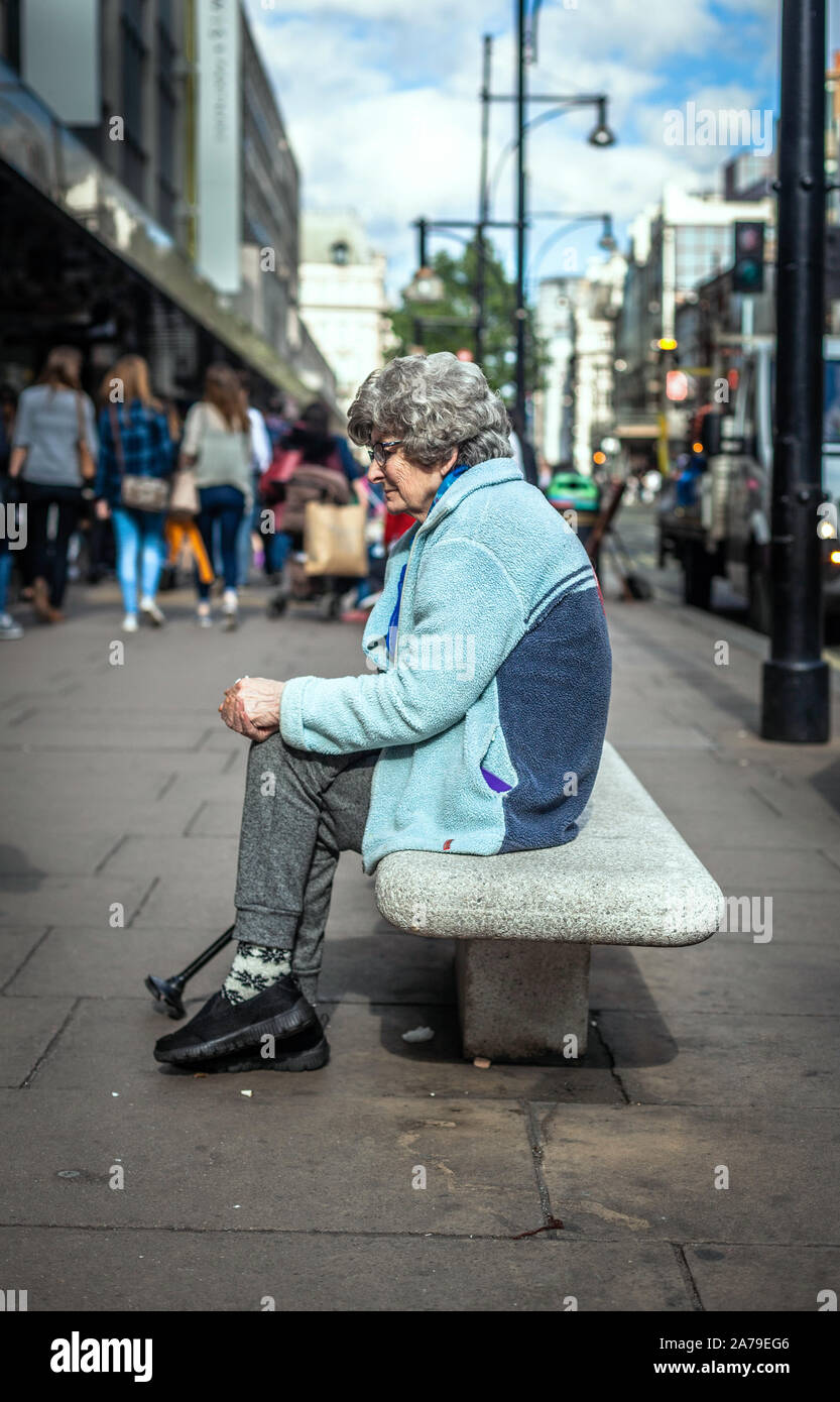 Ein Porträt einer alten Frau, die auf einer Straßenbank sitzt, Oxford Circus, London, England, Großbritannien. Stockfoto