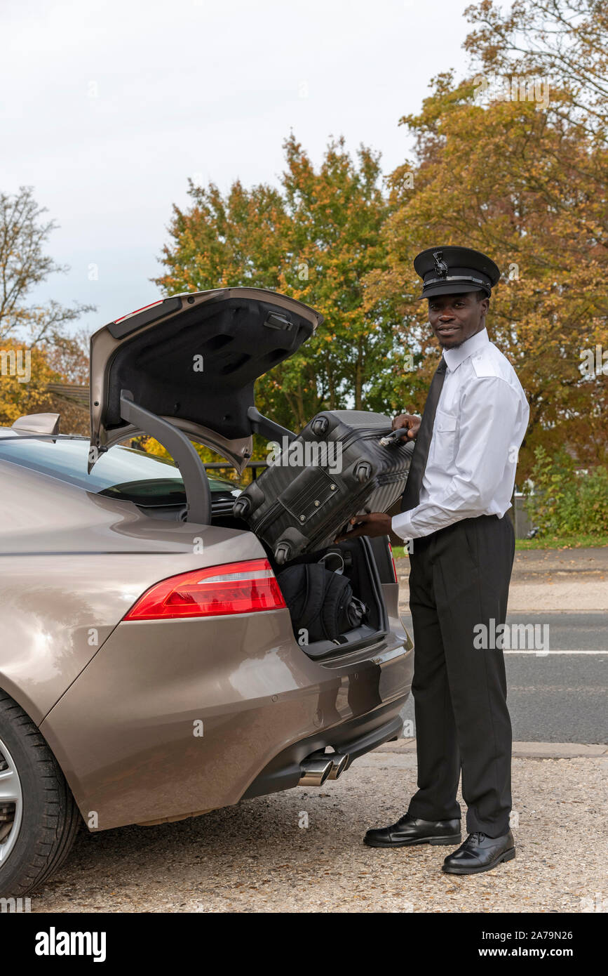 Andover, Hampshire, UK. Oktober 2019. Eine elegant gekleidete Chauffeur, Gepäck laden in den Kofferraum eines Luxus Auto. Stockfoto