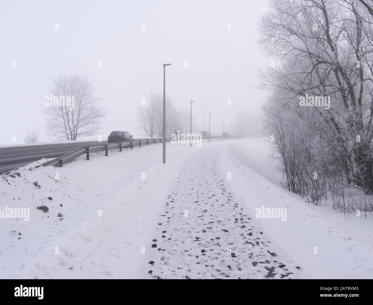 Straßenverkehr bei schlechten Sichtverhältnissen. Landschaft mit Nebel, eine verschneite Straße und die Bahn im Winter. Früh am Morgen, tagsüber ein Stunde. Stockfoto