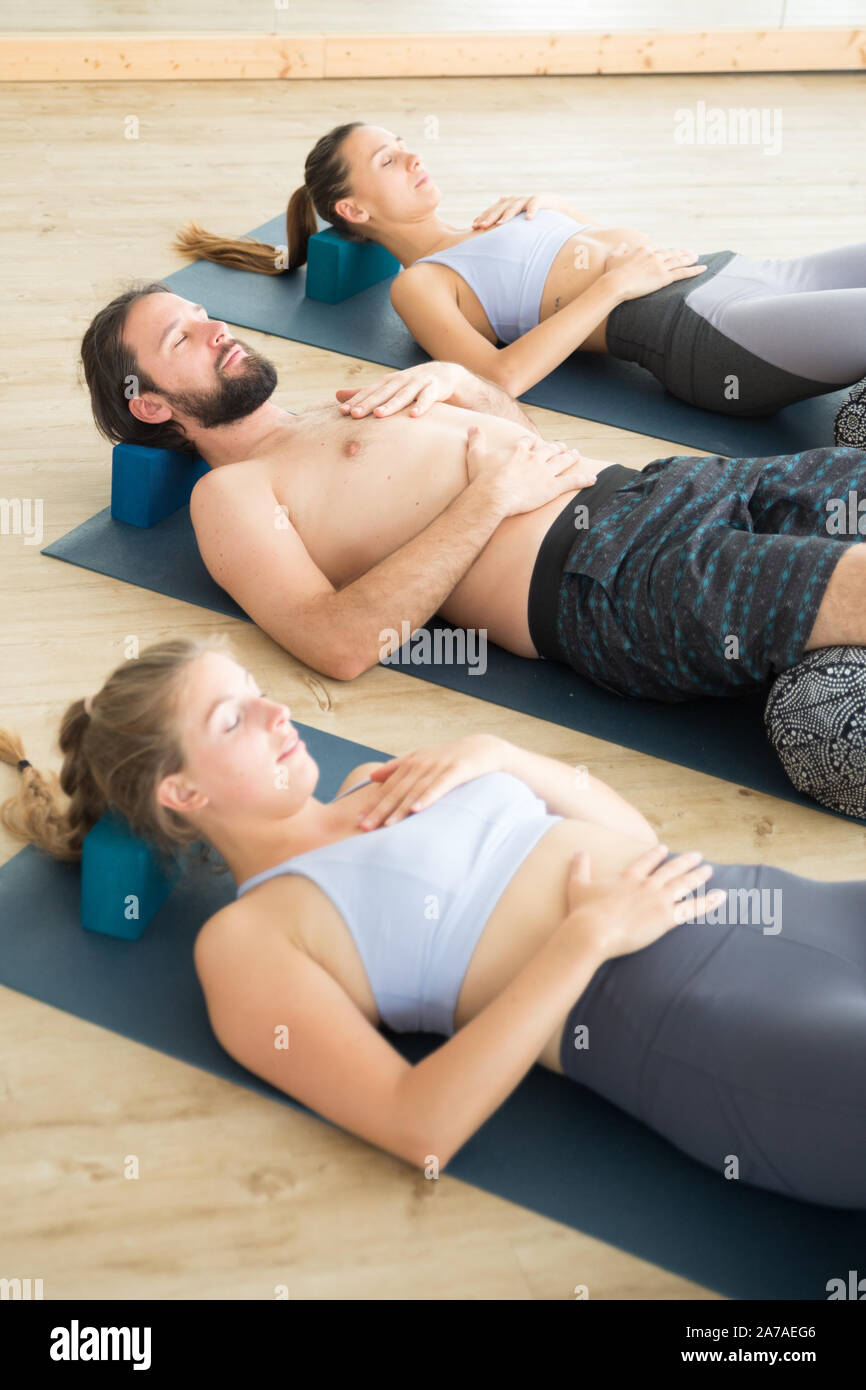 Restorative Yoga mit Polstern. Gruppe von jungen sportlich attraktive Menschen in Yoga Studio, liegen auf Kissen Polstern, Stretching und Entspannung Stockfoto