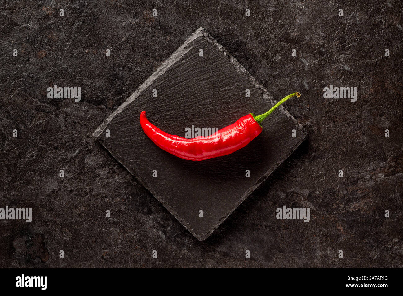 Einzelne rote getrocknete Banane Pfeffer auf einem dunkelgrauen Schiefer Stockfoto