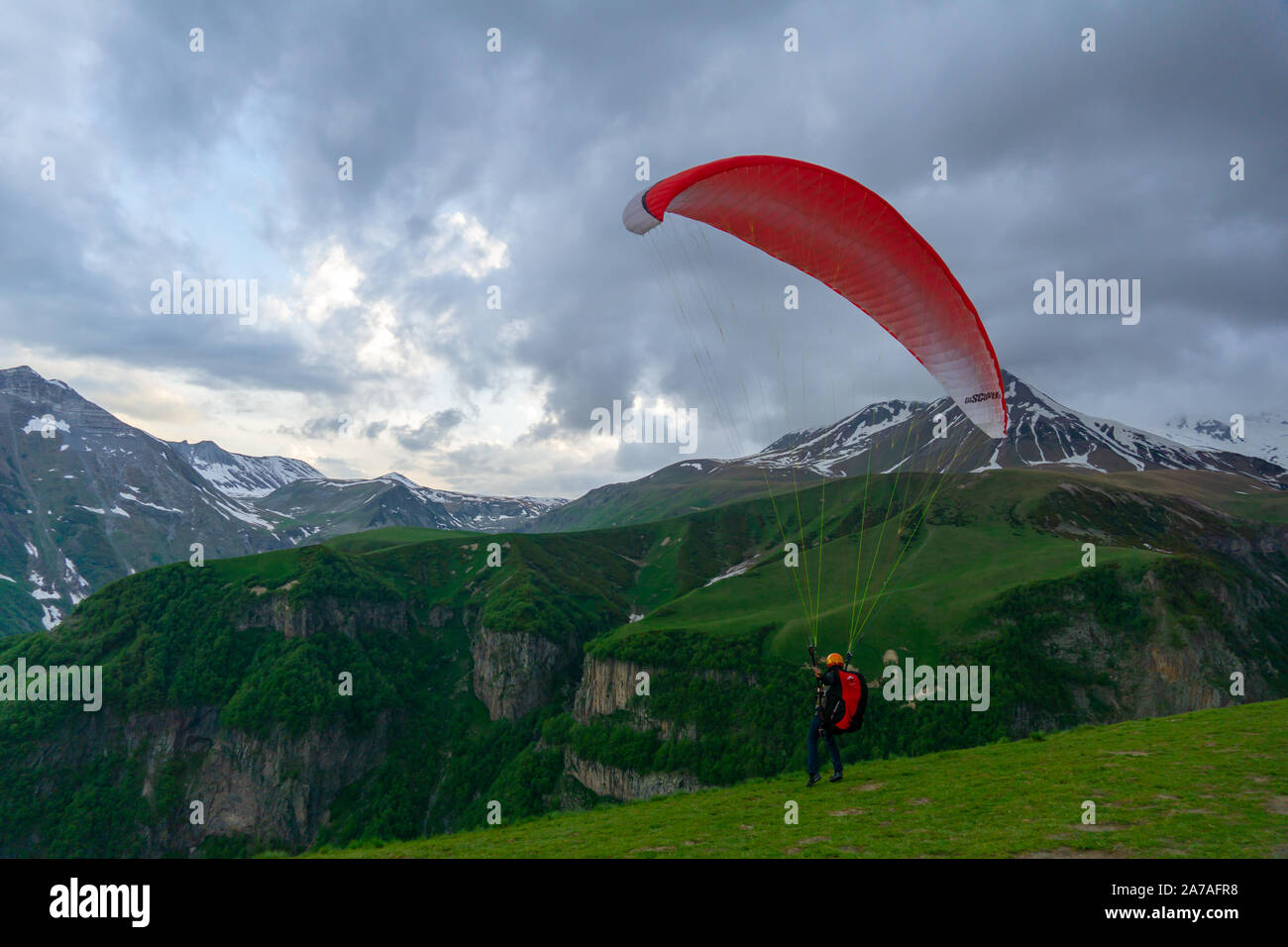 Gudauri, Kazbegi, Georgien: Menschen Paragliding durch den Teufel Tal im Kaukasus. Im Hintergrund die bunten Gipfel von Mount Kazbek Stockfoto