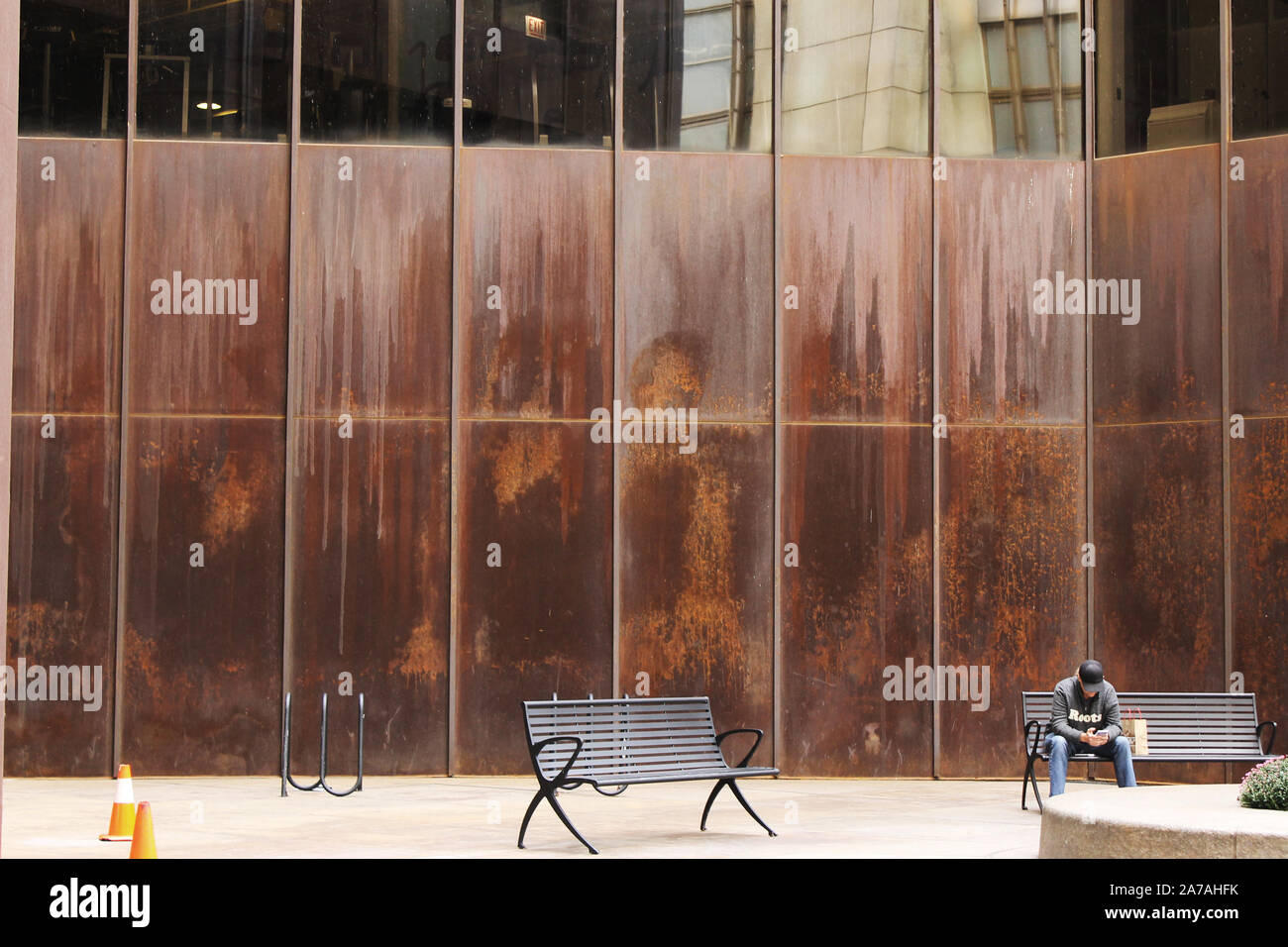 Ein Mann sitzt auf einer Bank vor einer hohen rostige Wand auf einem Condo-gebäude Stockfoto