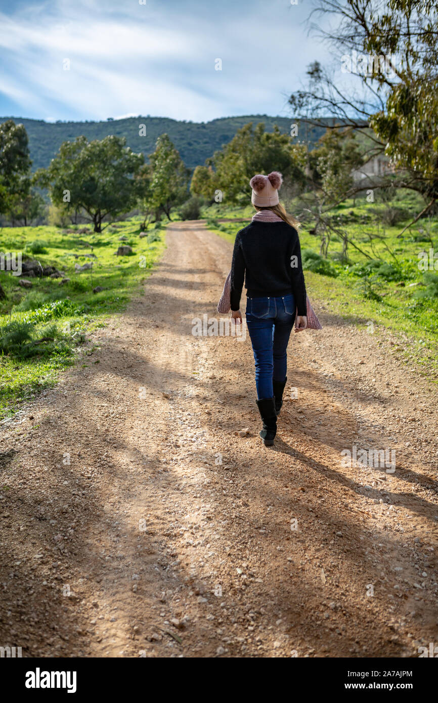 Ein Mädchen in einem rosa Hut mit Pompons und ein Schal Spaziergänge entlang einer Landstraße zu einer Bergkette Stockfoto