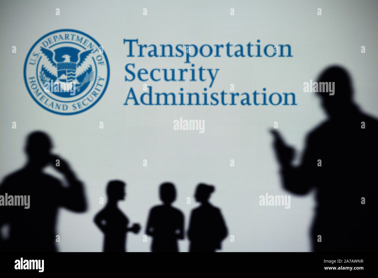 Transportation Security Administration Logo ist auf einem Bildschirm im Hintergrund, während eine Silhouette Person ein Smartphone verwendet (Redaktionelle Nutzung). Stockfoto