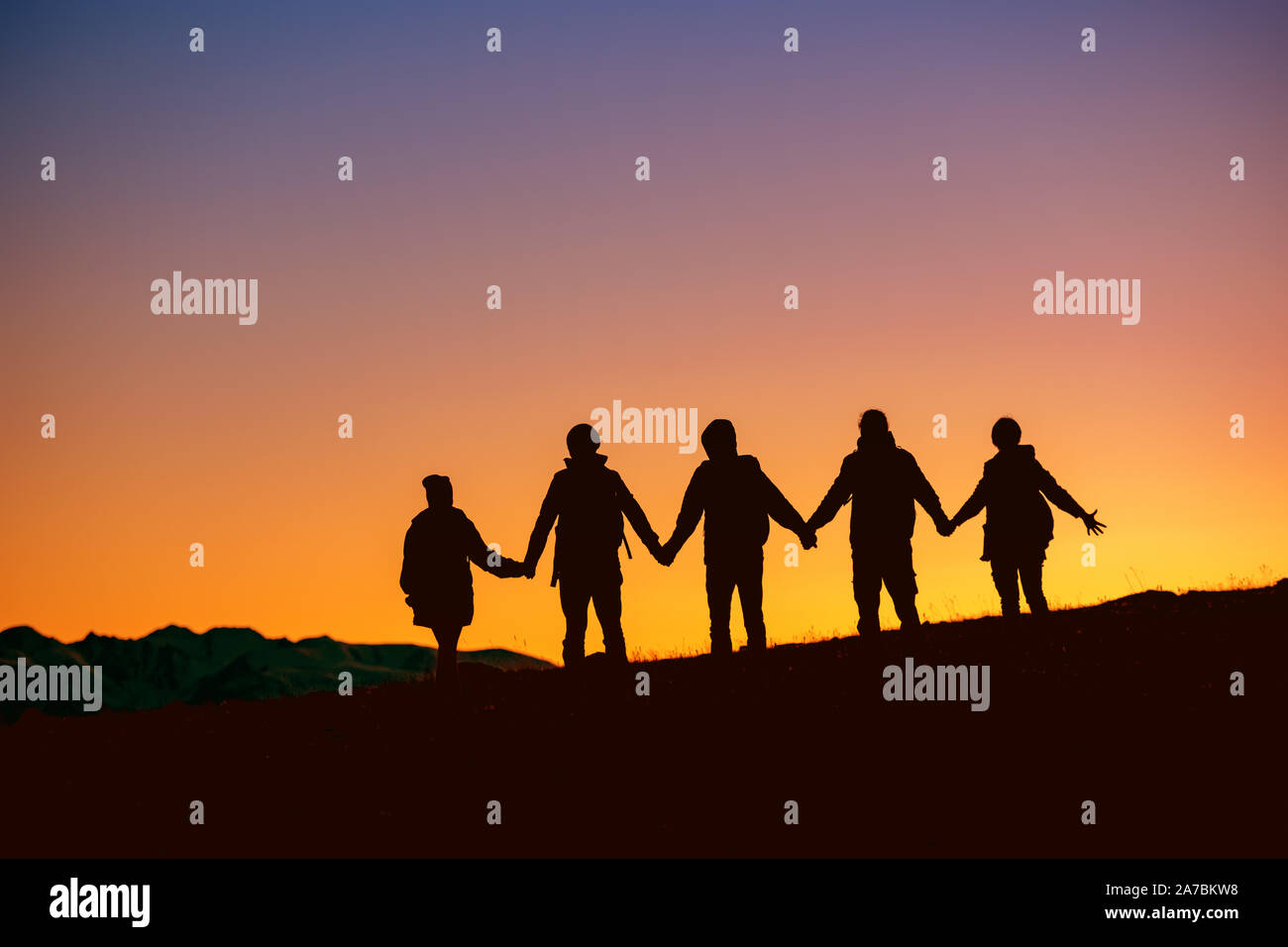 Silhouetten der Gruppe von Freunden zusammen bei Sonnenuntergang Zeit stehend gegen Berge Stockfoto