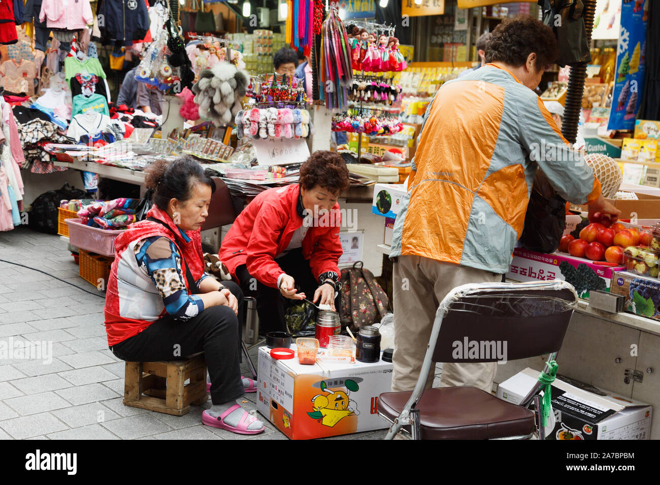 Die drei weiblichen stall Besitzer in kurzen gemeinsamen Mittagessen auf dem Karton als Tabelle durch ihre Geschäfte am Namdaemun Markt, Seoul, Südkorea. Stockfoto