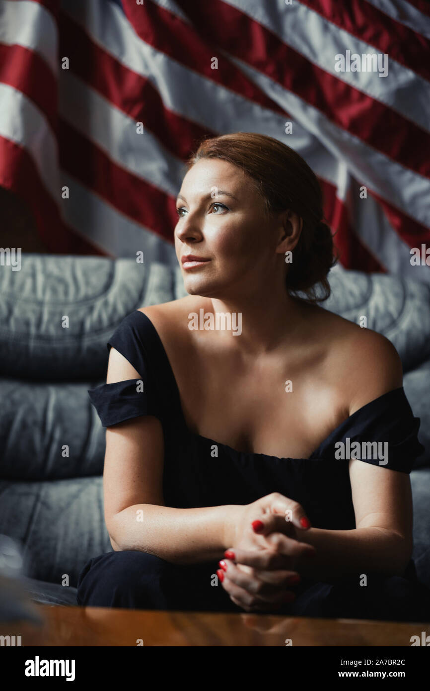 Stilvolle Frau sitzt auf einem Sofa vor der amerikanischen Flagge. Stockfoto