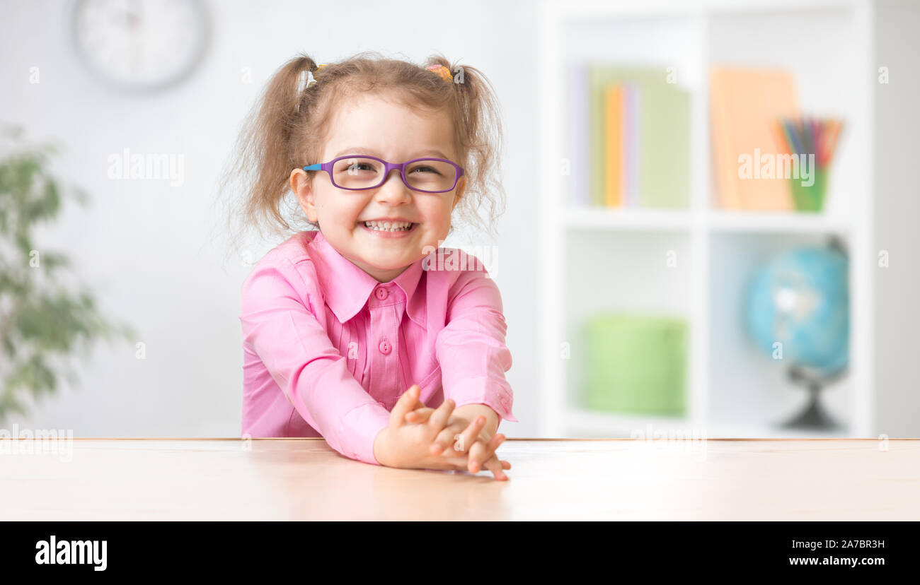 Glückliches Kind Mädchen in Brillen am Tisch sitzen Stockfoto