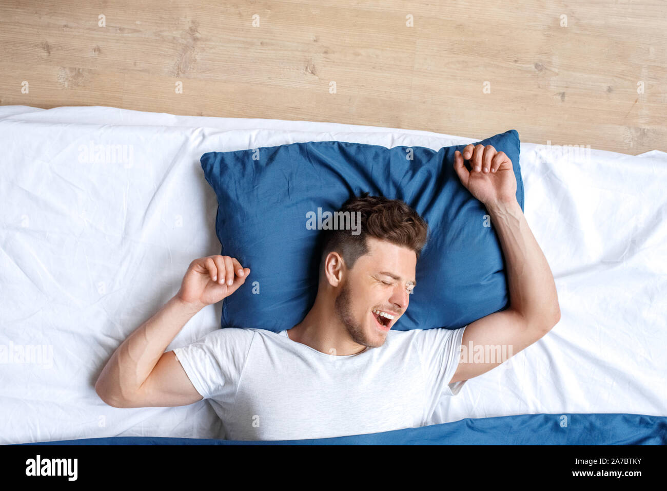 Junger Mann, liegend auf dem Bett vor dem Schlafengehen Draufsicht Aufwachen gähnen Stretching lächelnd Frohe Stockfoto