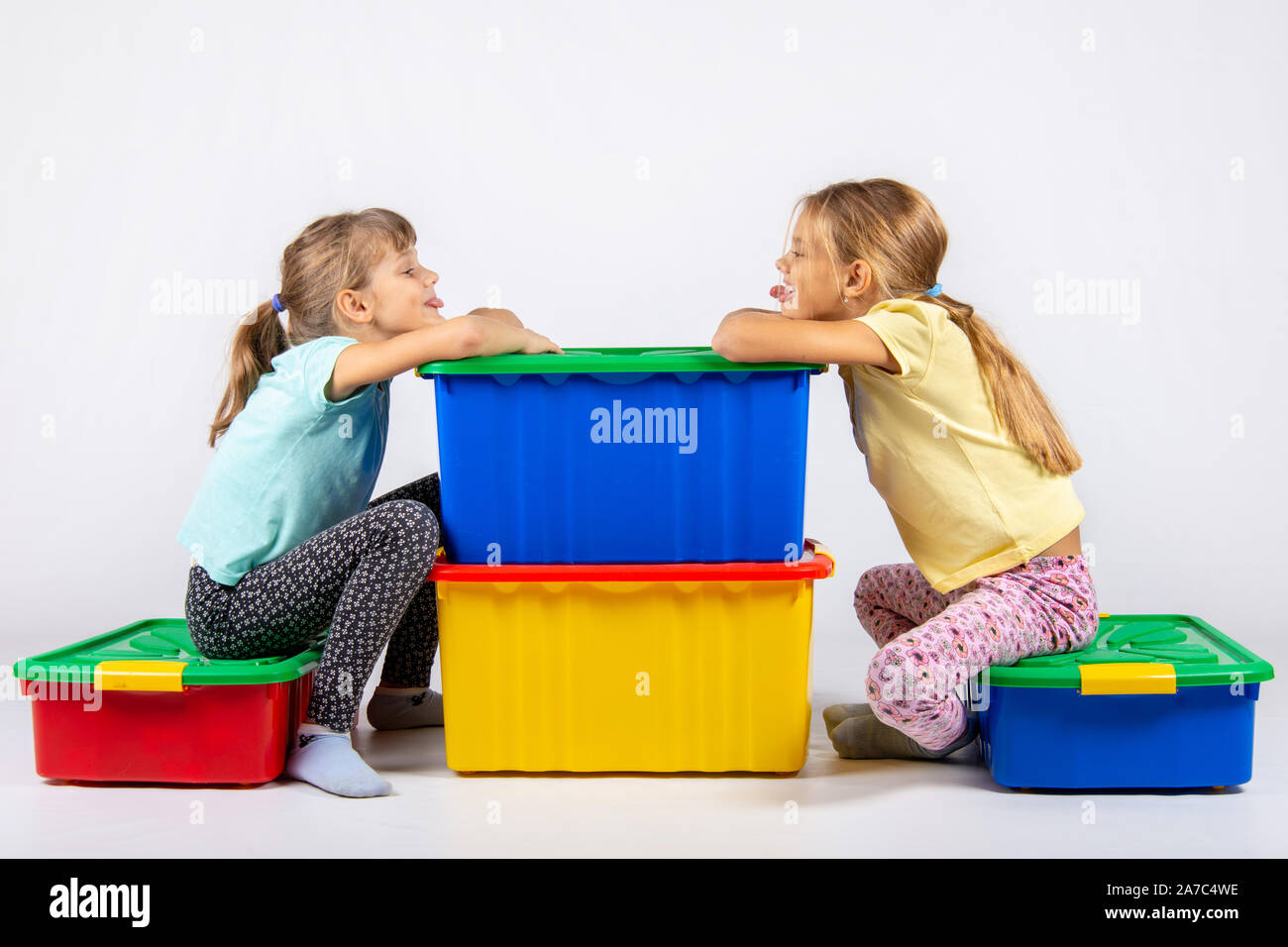 Zwei Mädchen sitzen auf großen Kartons für Spielzeug und jedes andere Zunge zeigen Stockfoto
