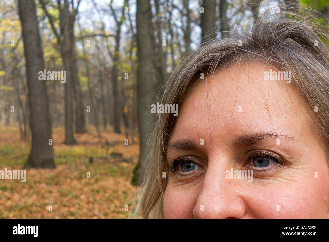 Gesicht Nahaufnahme von Frau mittleren Alters im Herbst Wald. Mädchen nicht an Kamera und lächelt auf unscharfen Hintergrund betrachten. Dachte, Meditation oder Zweifel expres Stockfoto
