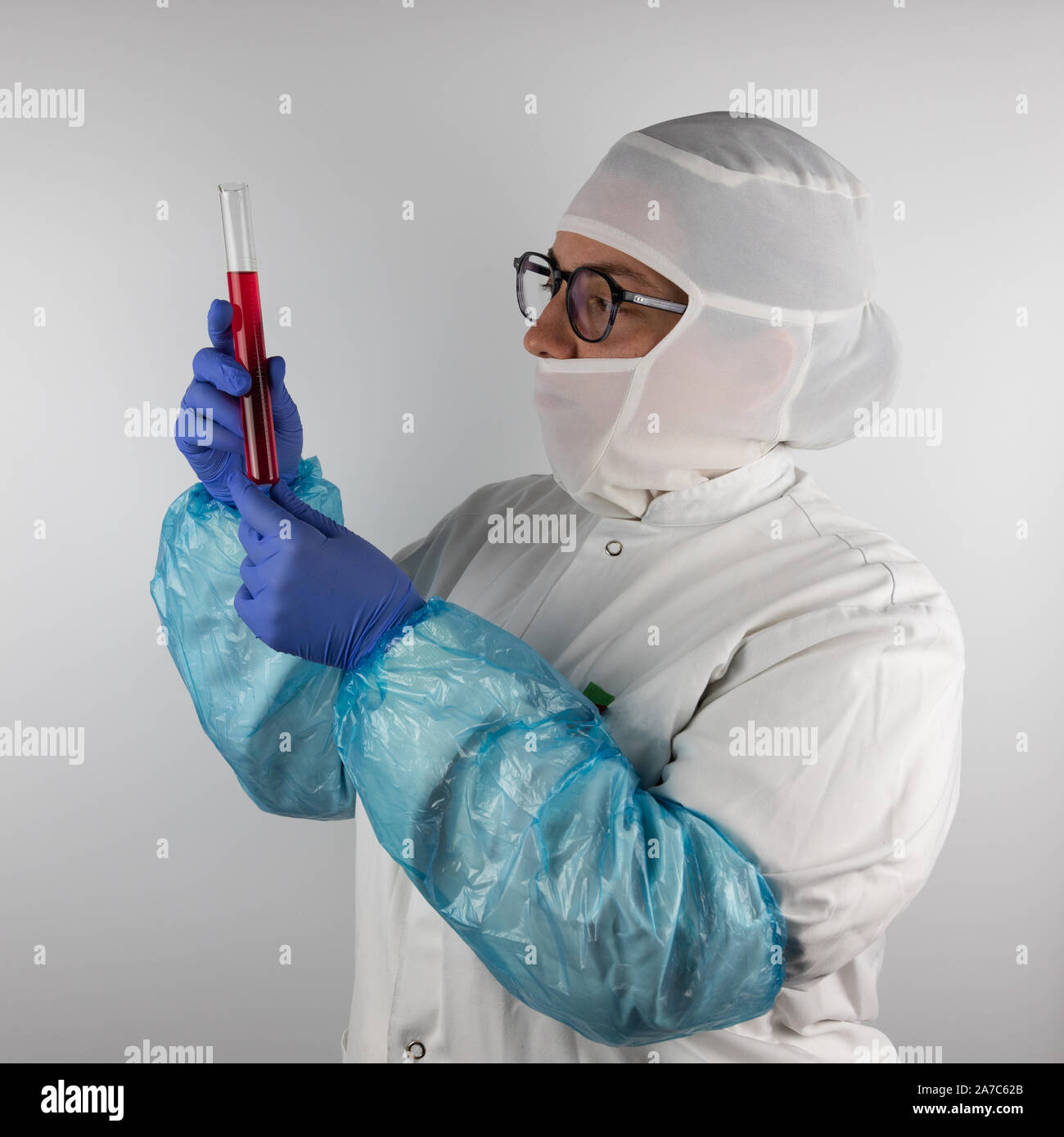 Junge Frau mit Brille, tragen weiße, sterile, Schutzkleidung und blaue Handschuhe, ein Rohr mit einer Probe, rote Flüssigkeit für die Lebensmittelindustrie Stockfoto