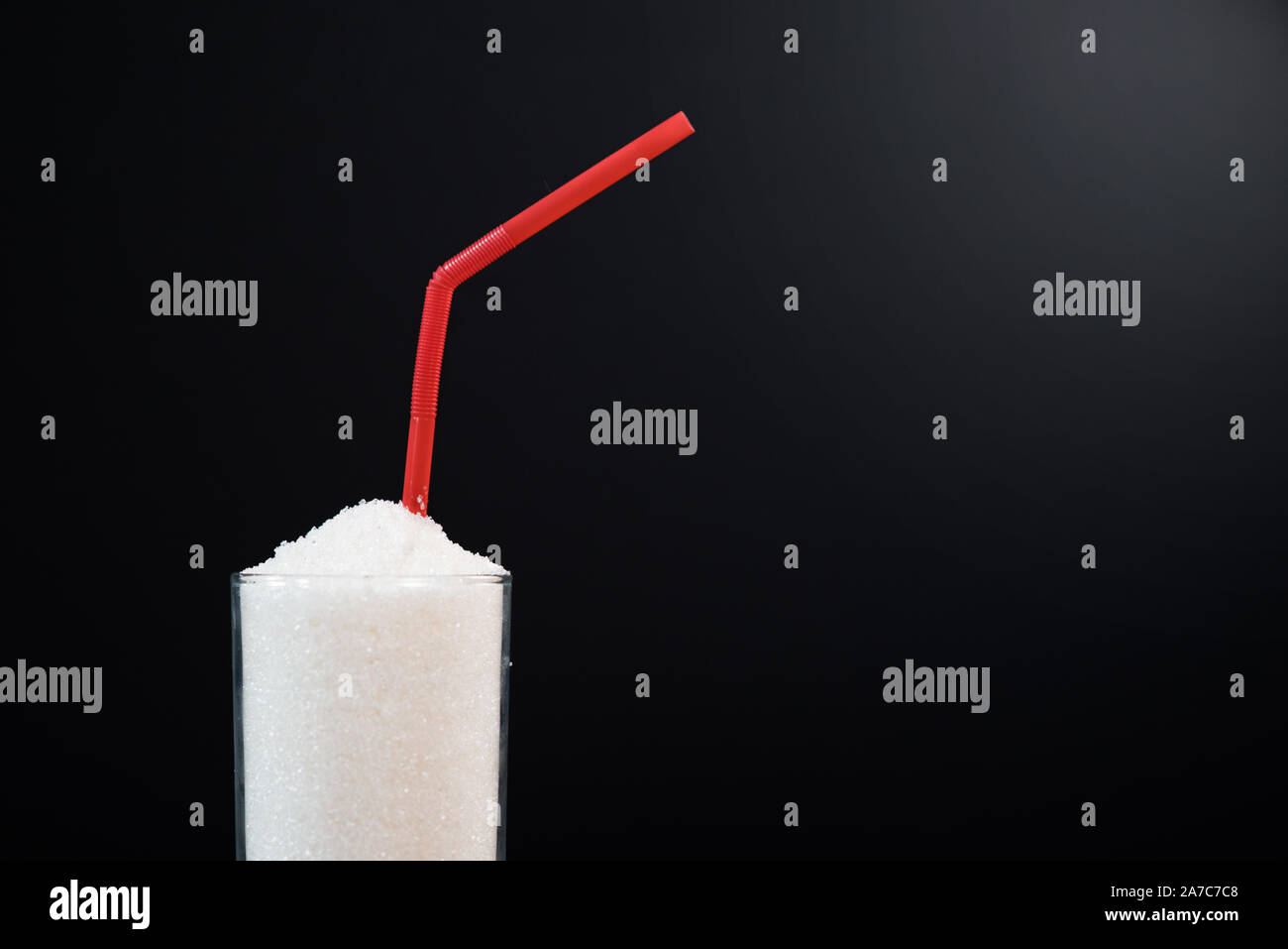 Ein Glas voll mit weißem Zucker mit Stroh auf schwarzem Hintergrund. Konzept der ungesunden Ernährung und diabetis Stockfoto