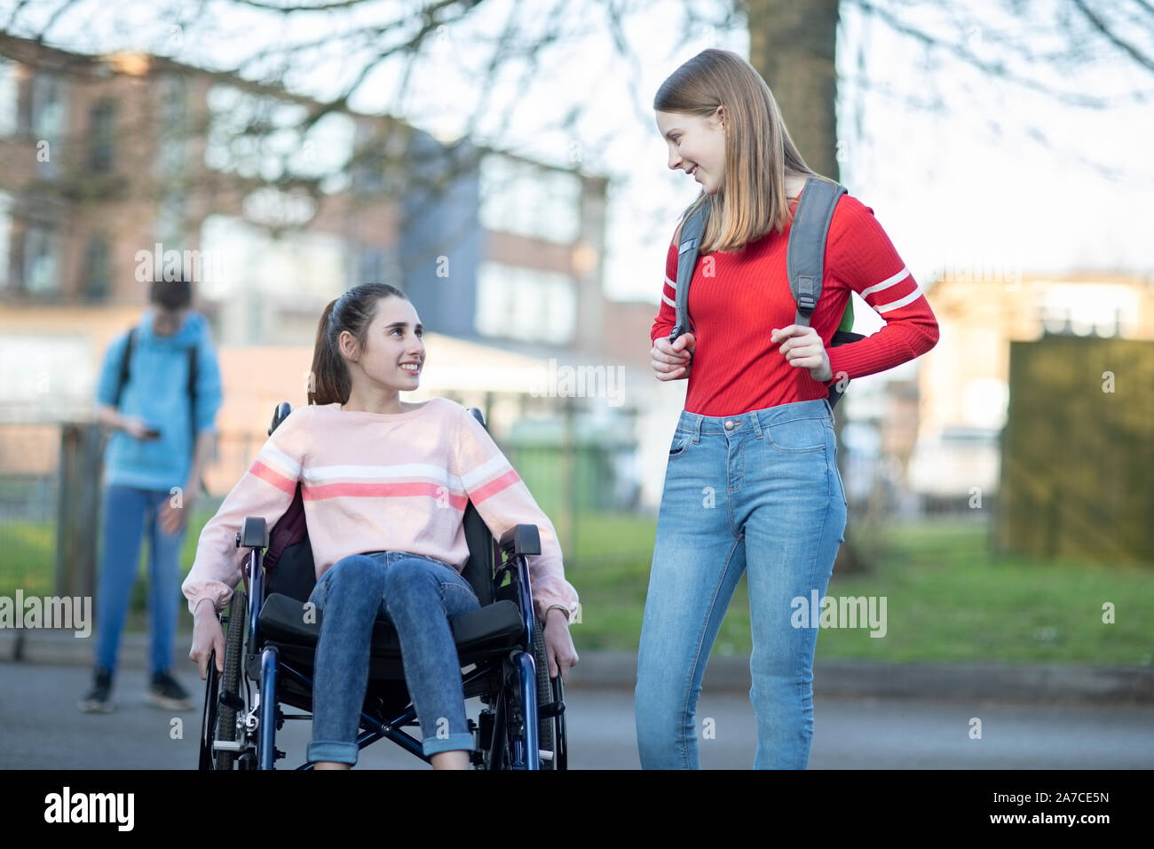 Teenage Mädchen im Rollstuhl im Gespräch mit Freund, als sie High School verlassen Stockfoto