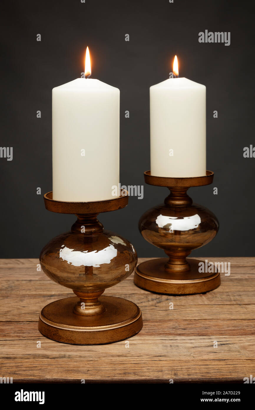 2 Bronze kerzenständer und leuchtende Kerzen, Schuß auf einen hölzernen Tisch, mit einem dunkelgrauen Hintergrund Stockfoto