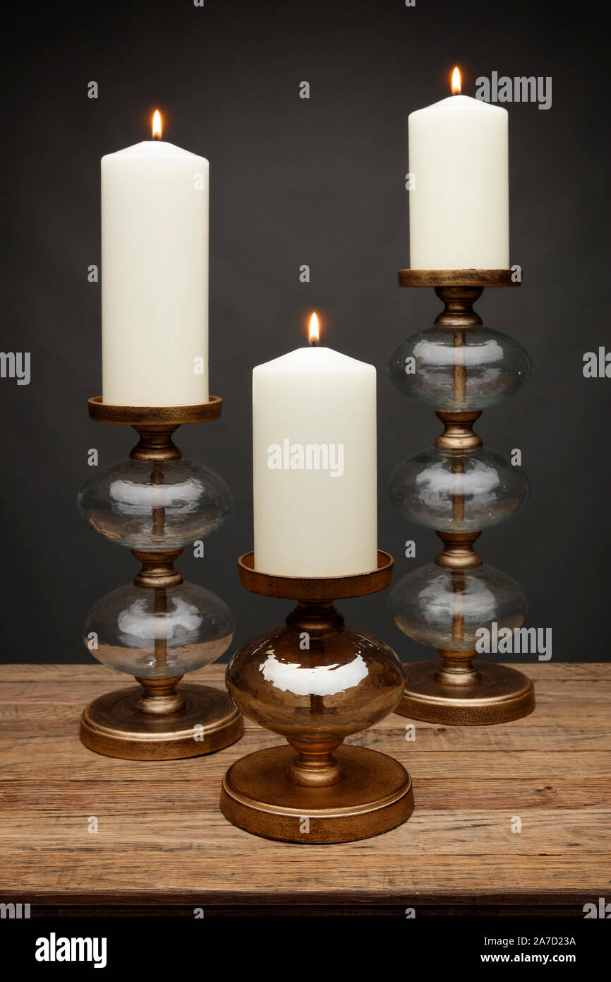 3 Glas Kerzenhalter und leuchtende Kerzen, Schuß auf einen hölzernen Tisch, mit einem dunkelgrauen Hintergrund Stockfoto