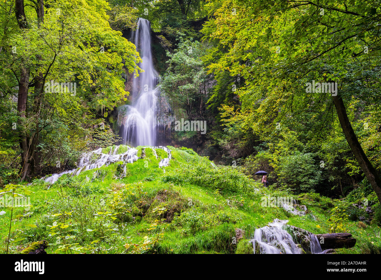 Deutschland, kleine Frau, die neben imposanten 37 m hohen Wasserfall der Luftkurort Region im grünen Wald von Bad Urach im schwäbischen Alb Natur landsca Stockfoto