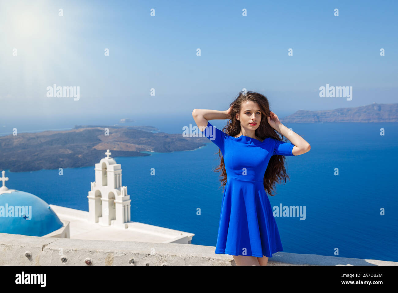 Schöne Frau mit langen schwarzen Haaren auf dem Hintergrund des Meeres und der Insel Santorini, Griechenland Stockfoto