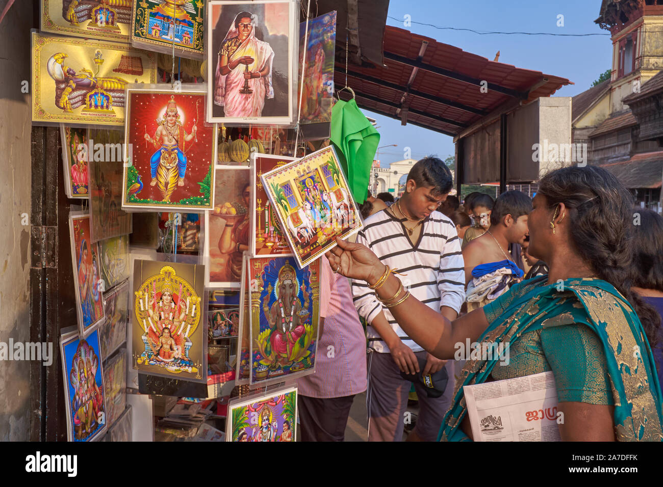 Bei einem Verkauf Abschaltdruck außerhalb Padmanabhaswamy Temple in Trivandrum, Kerala, Indien, eine Besucherin unter einer Anzahl von Bildern mit hinduistischen Gottheiten wählt Stockfoto
