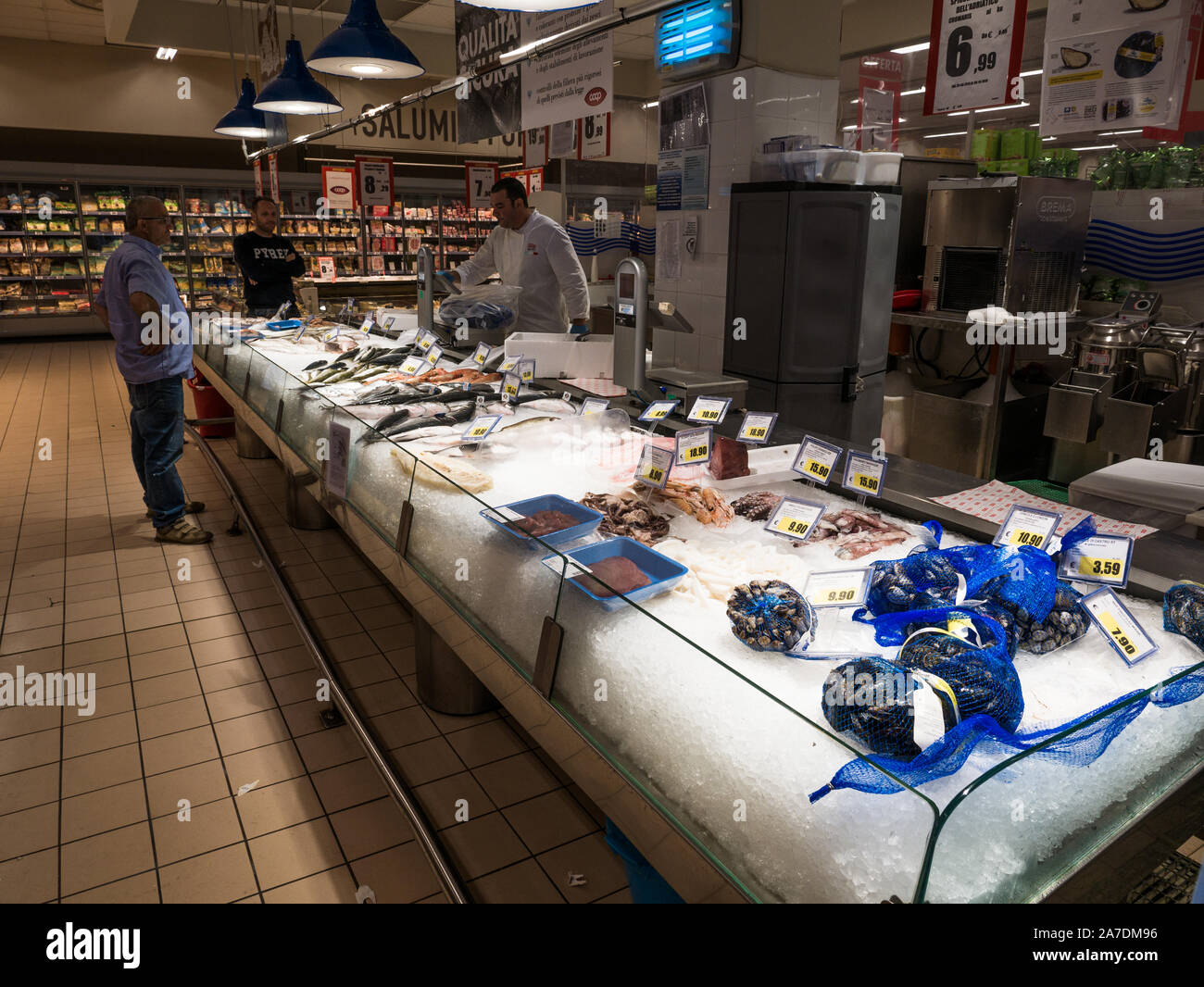 Tiefgekühlt iced Zähler mit frischen Fisch, Meeresfrüchte und Muscheln und mit Preis Etiketten in einer italienischen Supermarkt mit Verkäufer hinter der Bar Stockfoto