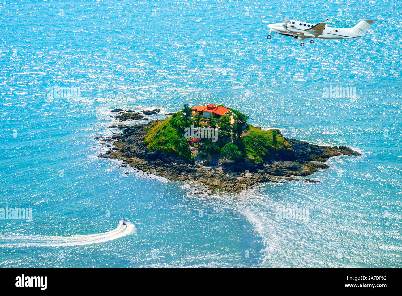 Oben auf einer kleinen Insel im Meer. Eine Private Jet fliegt in der Nähe und einen Jet ski schwimmt durch. Stockfoto