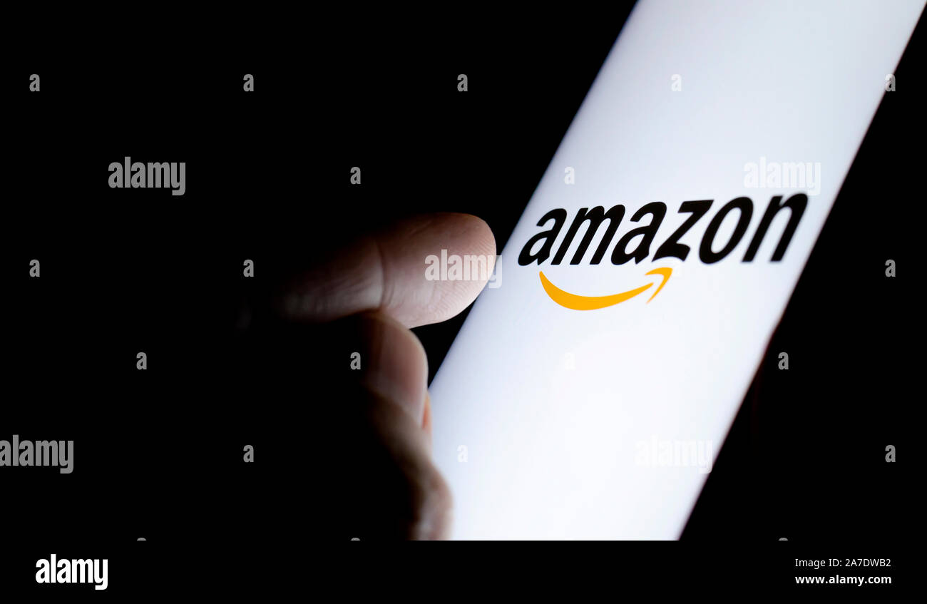 Amazon Logo auf einem Bildschirm des Smartphones in einem dunklen Raum und mit dem Finger auf sie zeigen. Stockfoto