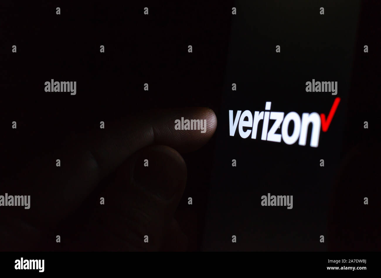 Verizon Logo auf einem Bildschirm des Smartphones in einem dunklen Raum und einen Finger zu berühren. Stockfoto