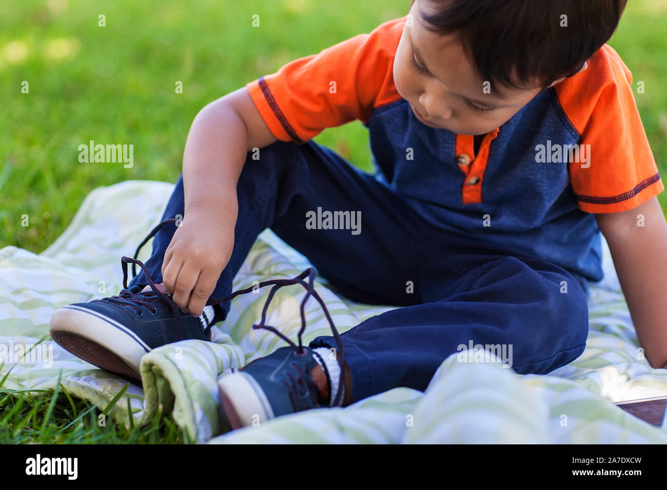 Eine nette junge lernen seinen Schuh zu binden, Schnürsenkel, und entspannen Sie in einem grünen Rasen. Stockfoto
