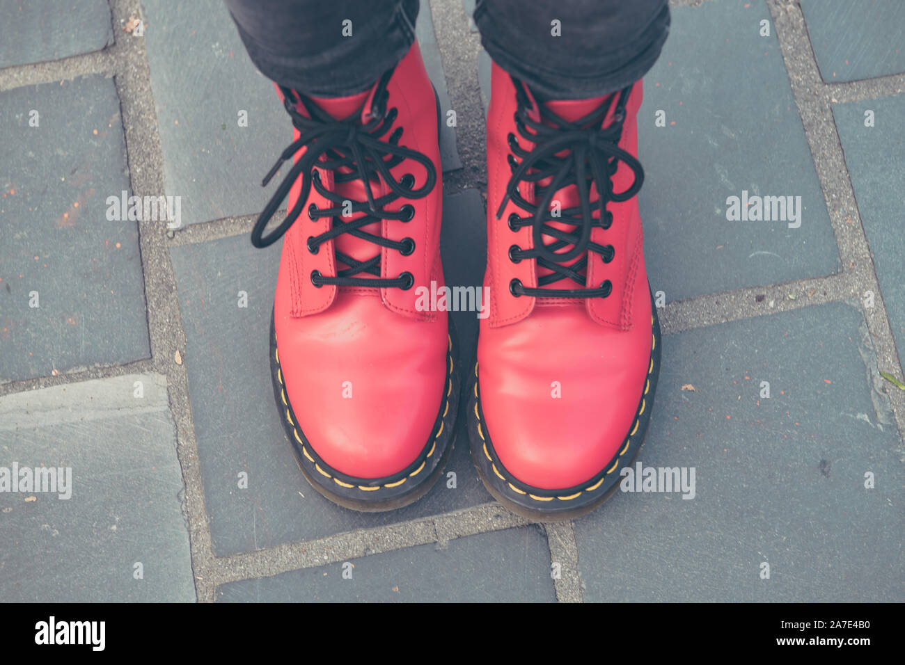 Mädchen steht mit neuen roten Stiefel, draußen auf einem Platz mit grauen Steinen. Stockfoto