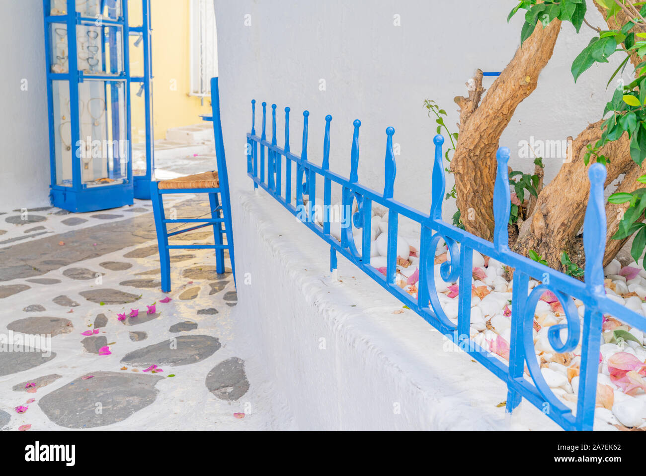 Innenhof mit blauen schmiedeeisernen Zaun, blauen Stuhl und verrückten Pflasterung und rosafarbene Bougainvillea Blüten auf Pfad. Stockfoto