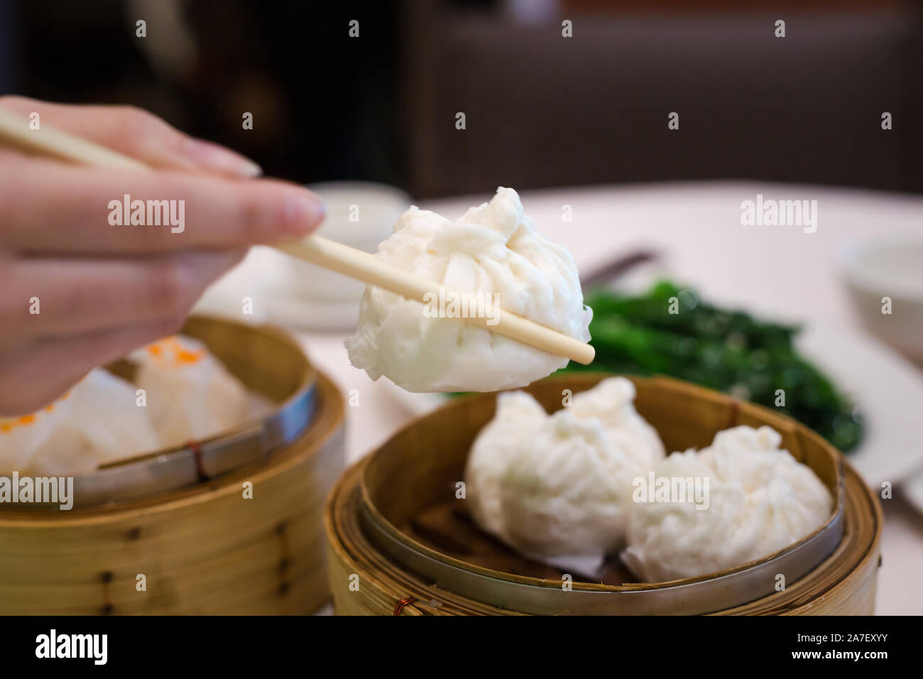 Eine Frau hält Essstäbchen und nimmt in einem Dim Sum Restaurant ein bbq-Schweinebun aus einem Bambusdampfer. Stockfoto