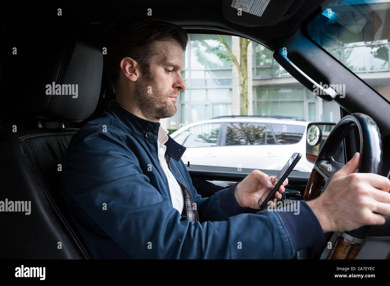 Ein Kaukasischer im mittleren Alter lenkte das Fahren ab, während er ein mobiles Gerät benutzte. Stockfoto