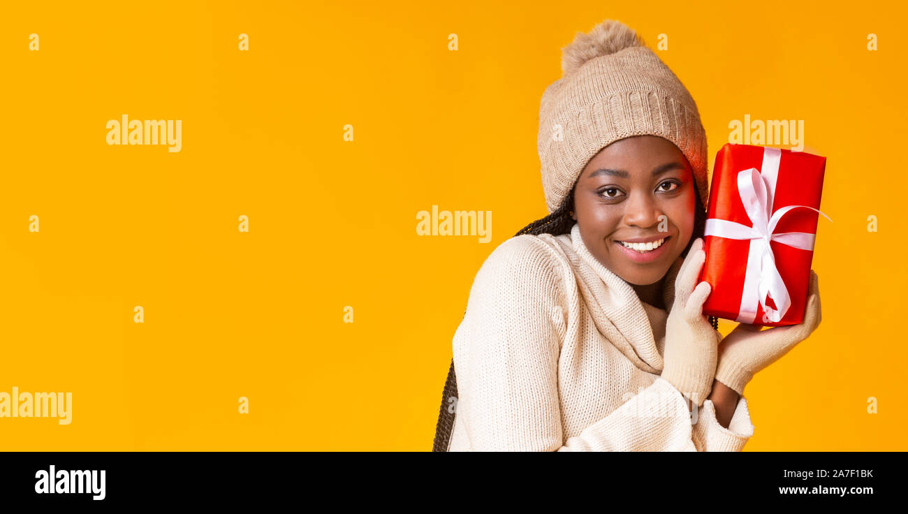 Hübsche schwarze Frau im Winter Mütze und Handschuhe holding Geschenk Stockfoto