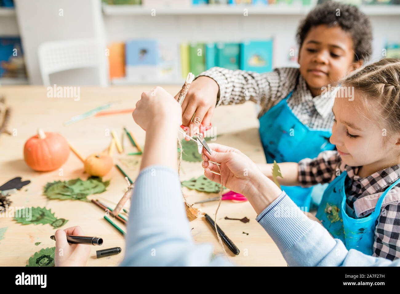 Cute Schüler schneiden Gewinde mit Schere, während seine Lehrer an der Lektion helfen Stockfoto