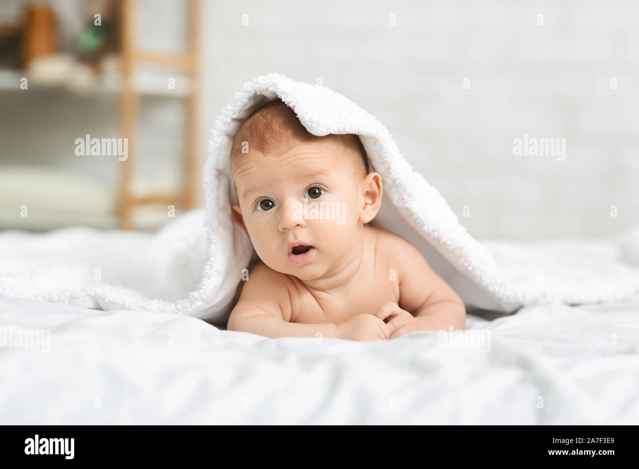 Niedlichen neugeborenen Jungen peeking unter weiche, weiße Decke Stockfoto