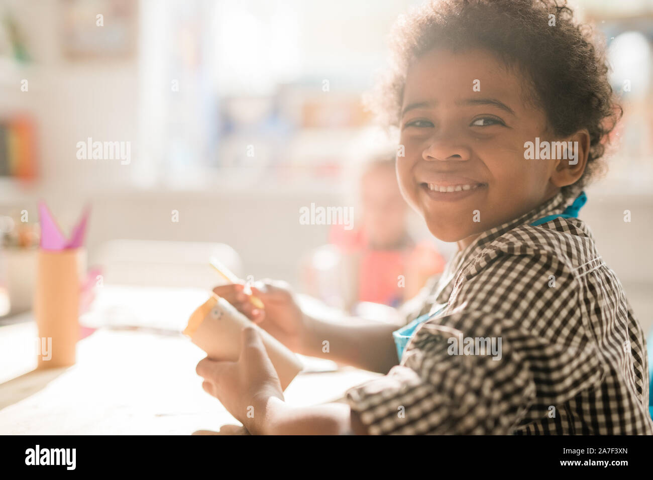 Freundliche Schüler mit gerolltem Papier, Sitzen, Schreibtisch, während Sie Dekoration Stockfoto