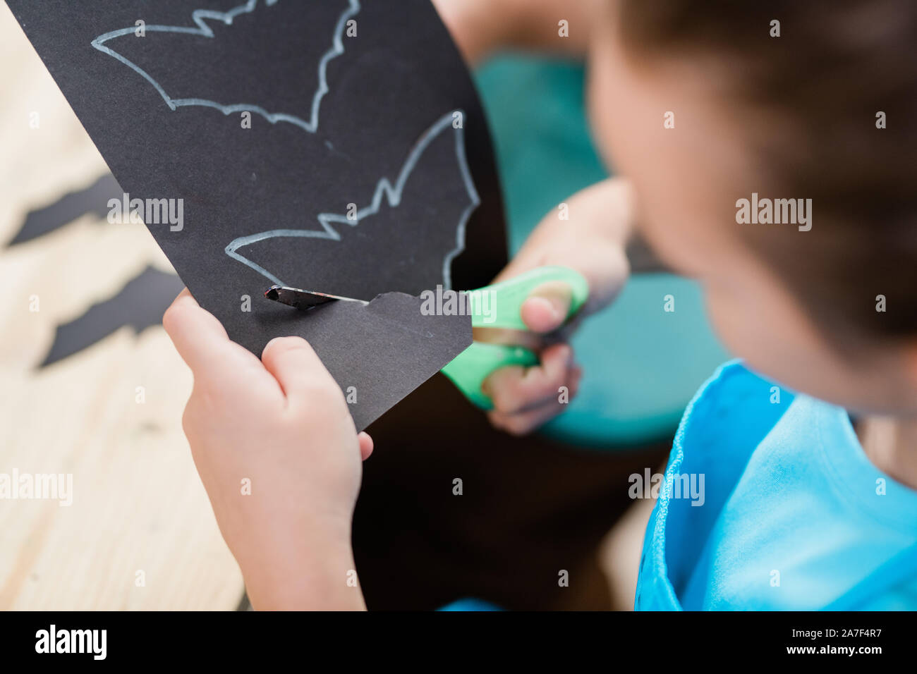 Hände von Elementrary Schulmädchen mit einer Schere ausschneiden bat aus schwarzem Papier Stockfoto