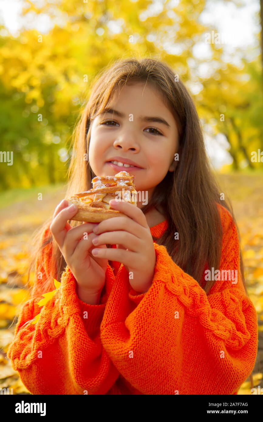 Kleines Mädchen in einem hellen orange Pullover bei einem Picknick in der Natur frisst ein leckeres Stück hausgemachten Kuchen Stockfoto