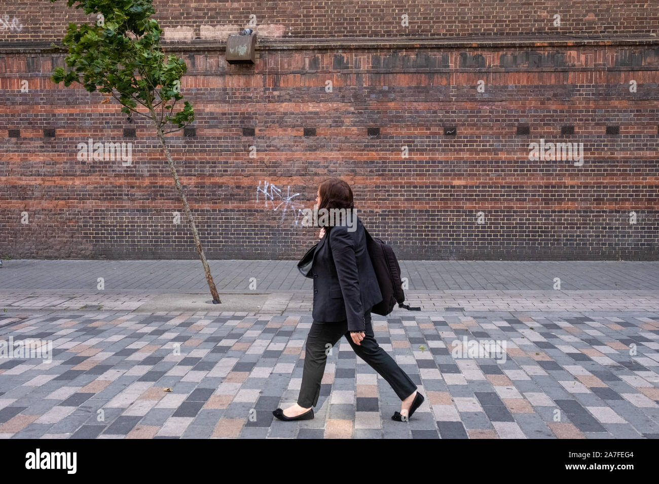 Eine Frau kämpft in der Brise in Camden Town. Ihr Haar ist, geblasen, wie der Baum im Bild ist. Stockfoto